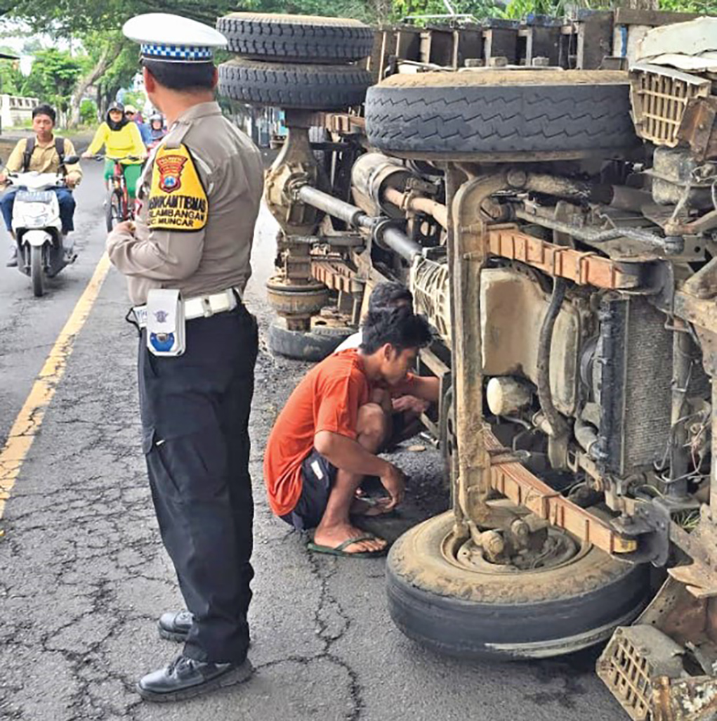 MUATAN BERAT: Mekanik memperbaiki ban truk yang terguling dengan pengawalan polisi.