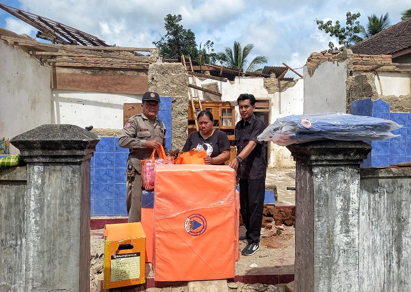 BANTUAN: Anggota BPBD Banyuwangi wilayah Kecamatan Songgon Abdul Hadi (kiri) menyerahkan bantuan ke Sri Rezeki didampingi staf kantor Desa Songgon kamis (8/5).