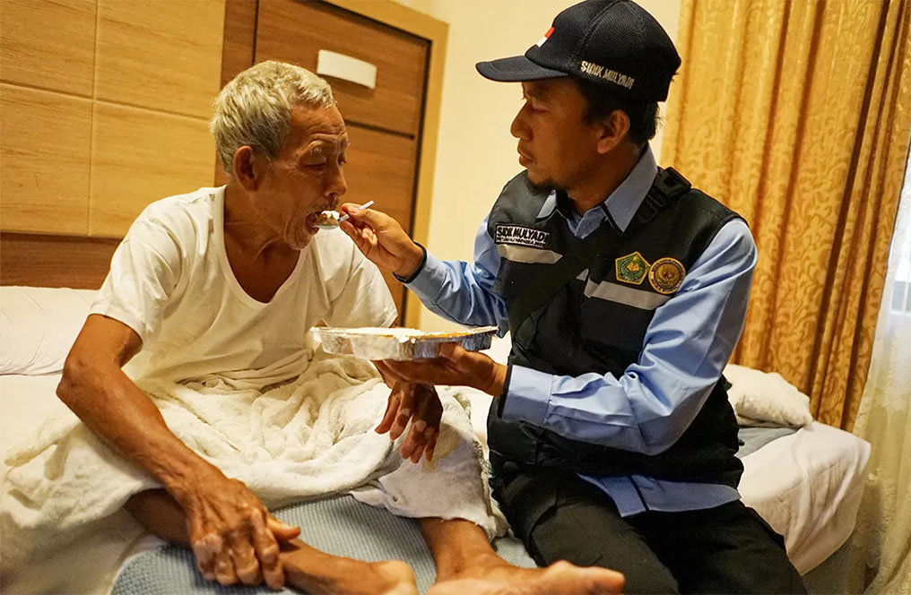 Tim Lansia, Disabilitas, dan PKP2JH PPIH Sidik Mulyadi menyuapi kakek yang masih belum bisa bertolak menuju Makkah karena kartu nusuknya belum keluar. (Dhimas Ginanjar/Jawa Pos)