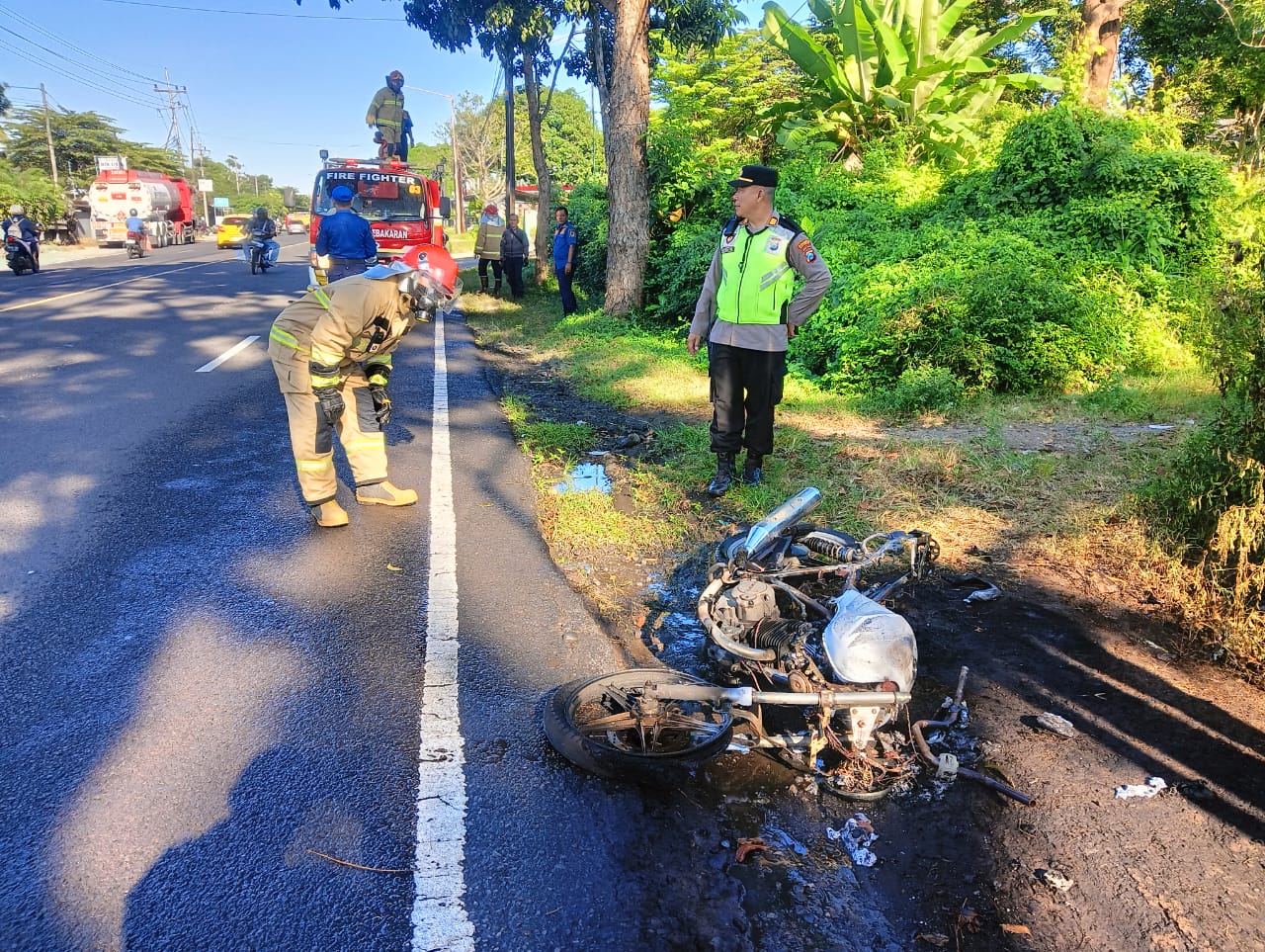 HANGUS: Kapolsek Kabat AKP Kusmin bersama anggota Damkarmat Banyuwangi memadamkan api yang membakar motor di tepi jalan raya di Desa Kedayunan, Kecamatan Kabat, Senin (21/7).