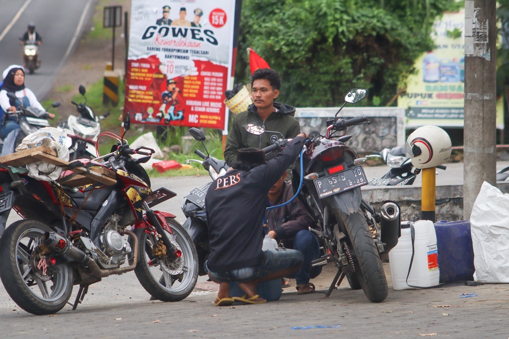 Pembeli asal Jember menyedot BBM dari tangki sepeda motor dan dipindah ke jeriken di depan SPBU Curahketangi, Desa Setail, Kecamatan Genteng , Selasa (9/7/2025).