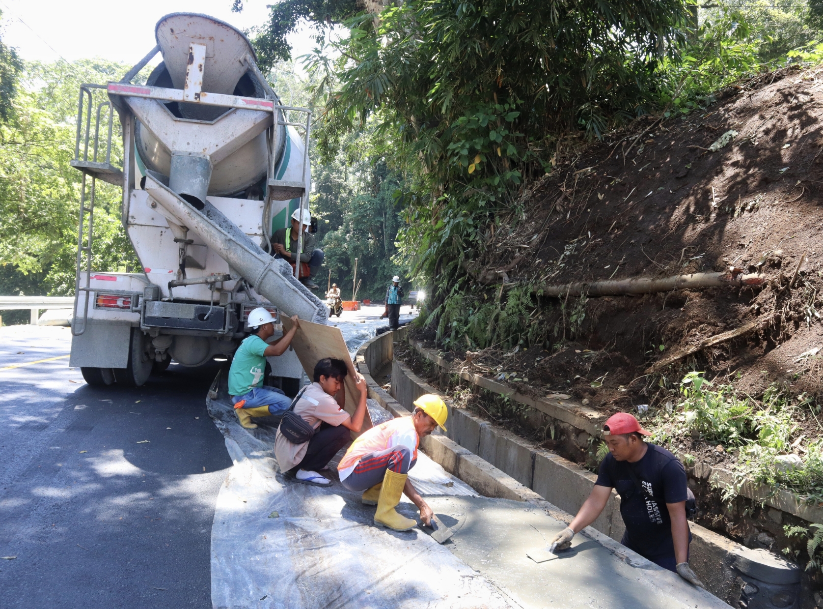 Pekerja di proyek Jalur Gumitir mengerjakan finishing dengan pengecoran bahu jalan.