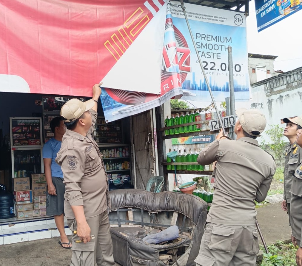 Petugas Satpol PP di Banyuwangi sedang mencopot baliho rokok di warung-warung.