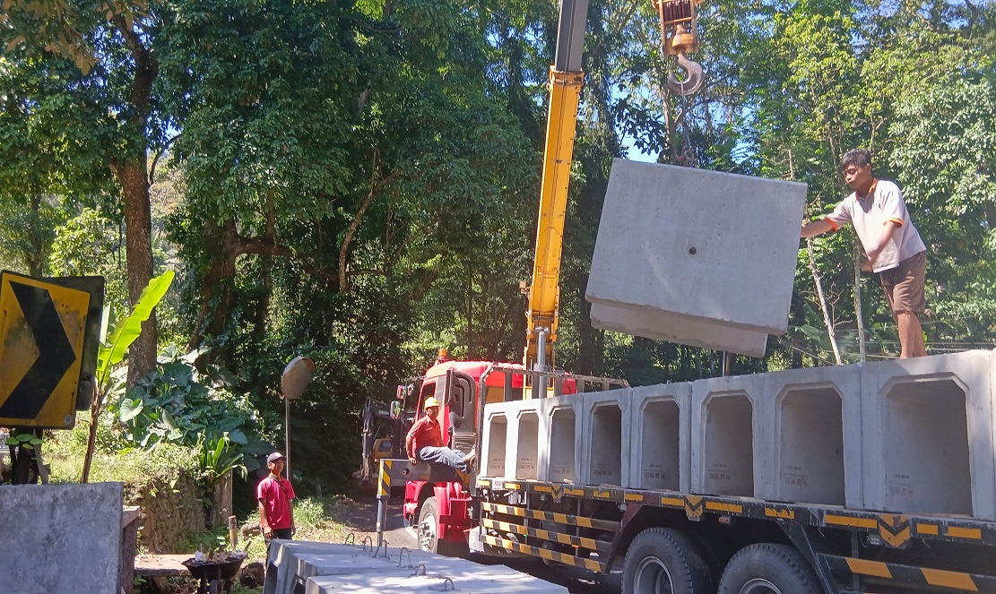 Pekerja proyek menurunkan U-ditch untuk dipasang sebagai saluran di Jalur Gumitir KM 229.