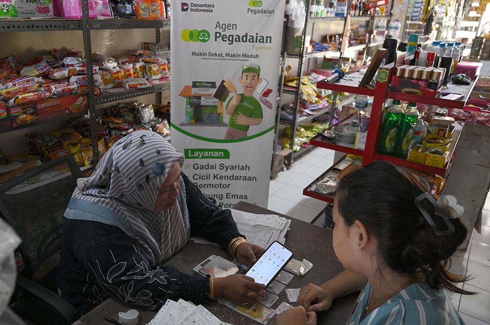 Sumiyati (47), Agen Pegadaian Toko Buksum di Desa Pesucen, Kecamatan Kalipuro, Kabupaten Banyuwangi menunjukkan fitur tabungan emas di aplikasi Tring by Pegadaian kepada calon nasabah yang datang ke tokonya, Sabtu (11/10/2025). Sembari menata emas-emas ba