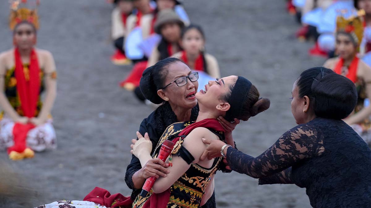 Dua penari gandrung senior melakukan ritual Meras Gandrung di Pantai Boom Banyuwangi. Seorang penari berbaring di atas pasir, lalu dibacakan doa-doa oleh dua penari senior.