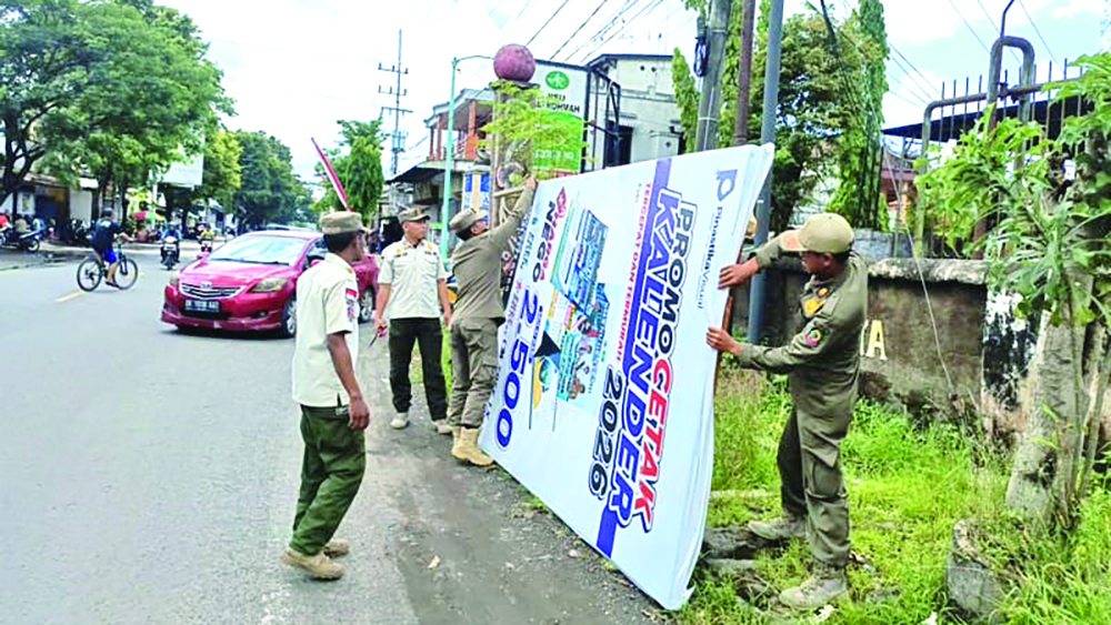 Petugas Satpol PP menertibkan reklame yang habis masa aktifnya atau kedaluwarsa di Dusun Kampung Baru, Desa Jajag, Kecamatan Gambiran, Rabu (12/11).