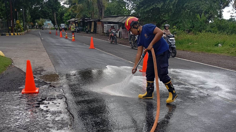 PEMBERSIHAN: Tim Damkarmat Sektor Srono membersihkan tumpahan solar yang tercecer di jalan raya Benelan Kidul, Kecamatan Singojuruh, Jumat (15/11).