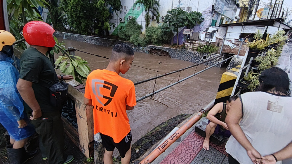 Sejumlah warga memantau debit air Sungai Bagong dari atas jembatan saat hujan deras, mengguyur kawasan kota Banyuwangi, Rabu (19/11).
