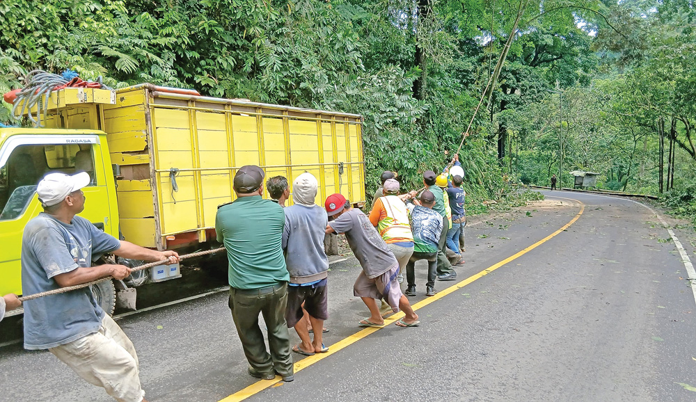 Petugas gabungan dari unsur relawan dan kepolisian gotong royong menarik dahan pohon rawan roboh di tepi jalan raya di Gunung Gumitir.
