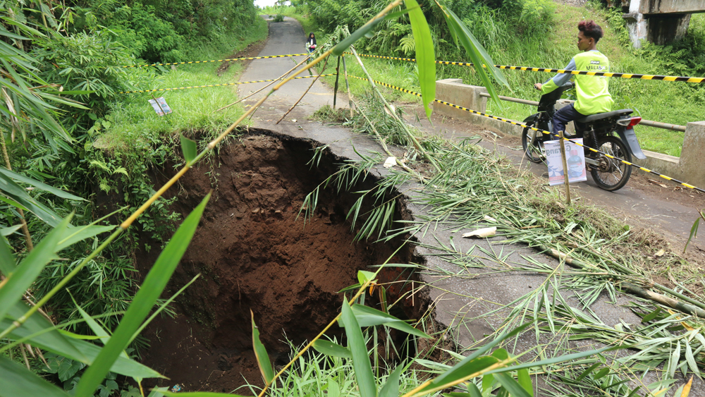 Warga melintasi jembatan yang ambrol di Dusun Krajan, Desa Kajarharjo, Kecamatan Kalibaru pada Jumat lalu (28/11).