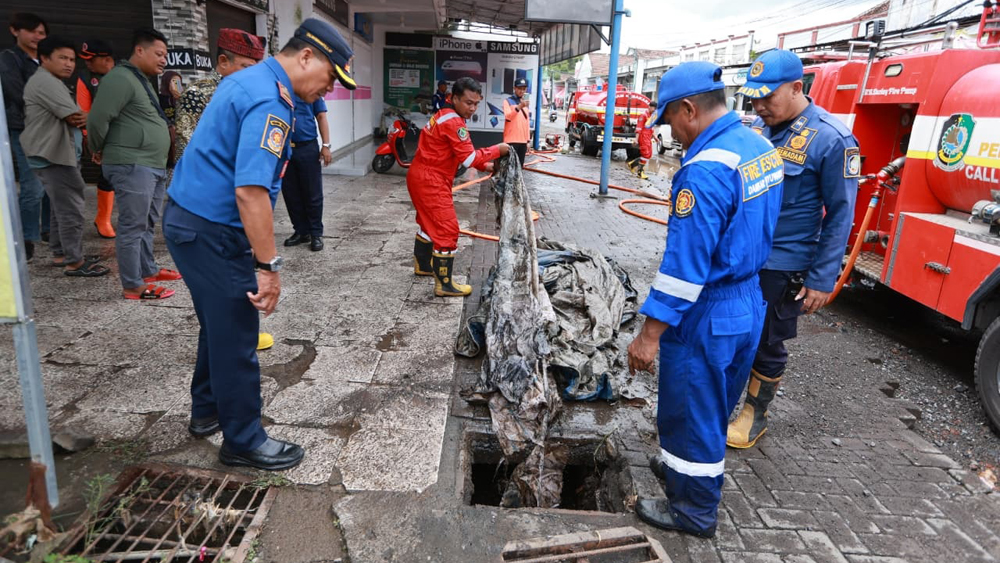 Petugas Damkarmat membersihkan gorong-gorong sungai yang tersumbat terpal.