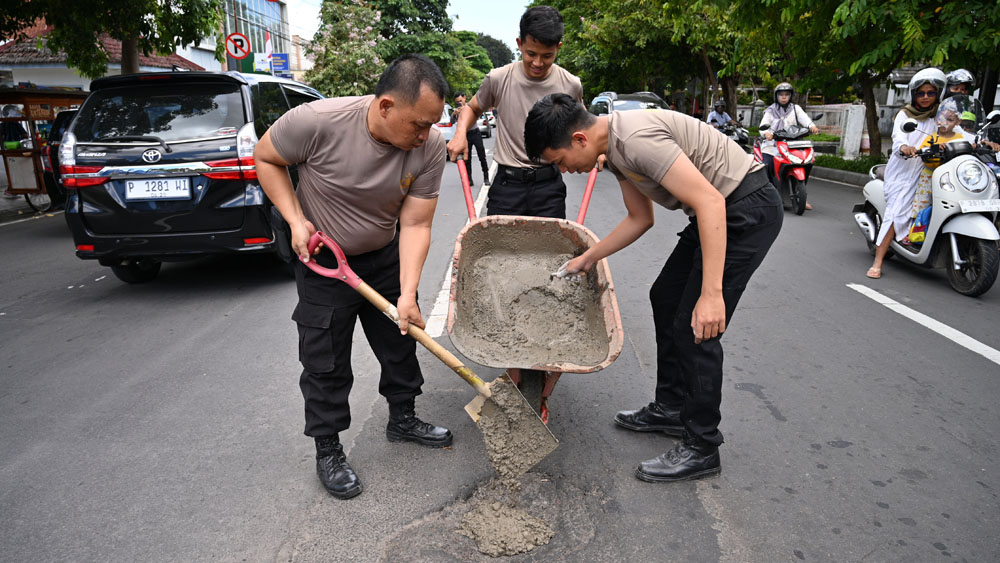 Personel Polresta Banyuwangi menambal jalan berlubang memakai campuran pasir, koral, dan semen di Jalan Ahmad Yani, depan kantor Kecamatan Banyuwangi, Selasa (3/2).