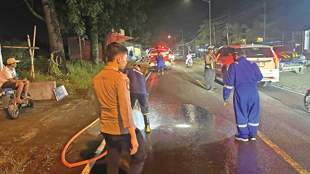 Petugas Damkarmat Sektor Genteng menyemprot badan jalan untuk membersihkan tumpahan solar pada Rabu malam (11/2).