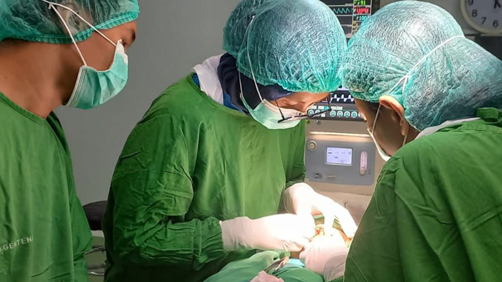 Dokter spesialis bedah mulut melakukan penjahitan luka pada rongga mulut pasien yang luka akibat trauma.