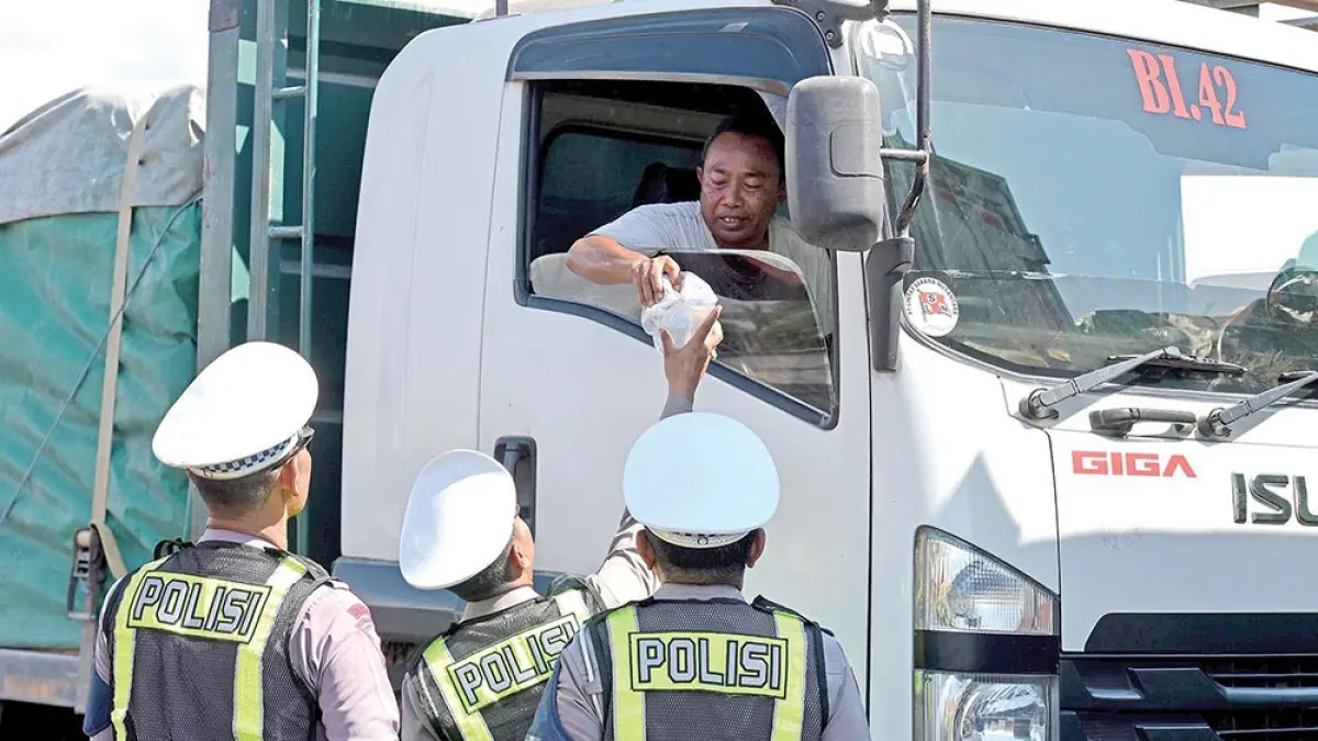 PEDULI SOSIAL: Personel Satlantas Polresta Banyuwangi membagikan nasi bungkus kepada driver yang antre masuk kapal di Pelabuhan Ketapang, Minggu (5/4). (Ramada Kusuma/Radar Banyuwangi)
