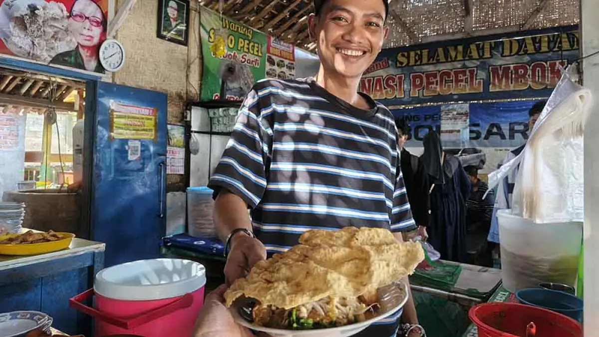 PEYEK OMBO: Bagus, cucu menantu Mbok Sarti,  menyajikan nasi pecel dengan lauk rempeyek di warungnya yang beralamat di Desa Sumberberas, Kecamatan Muncar. (Zamrozi Wahyu/Radar Banyuwangi)