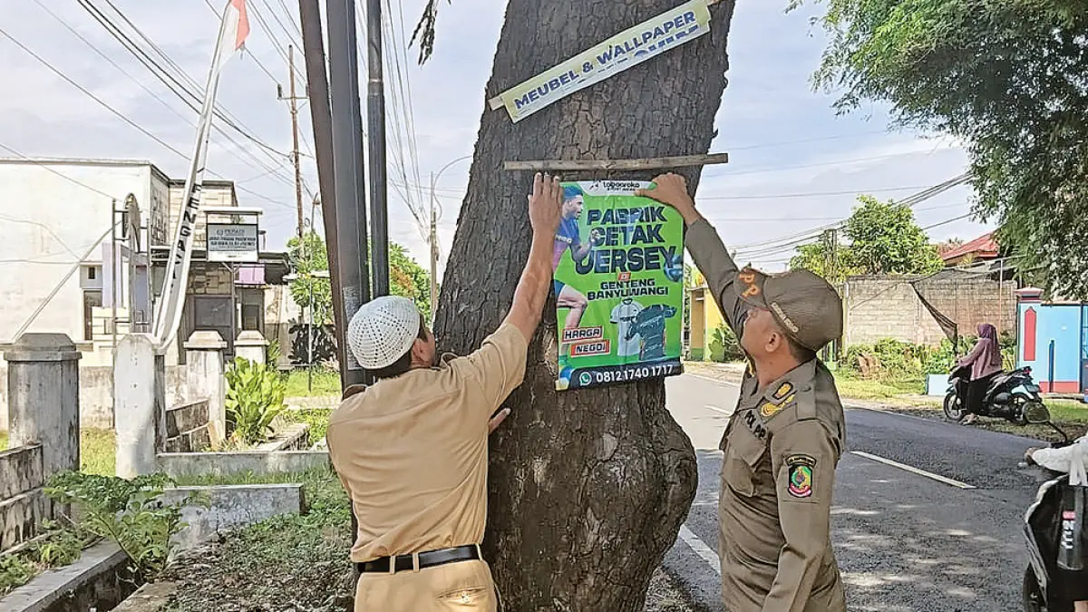 PENERTIBAN: Petugas mencopot reklame ilegal dan kedaluwarsa yang masih terpasang di sepanjang jalan nasional di wilayah Kecamatan Cluring pada Senin selumbari (20/4). (Subhani for Radar Banyuwangi)