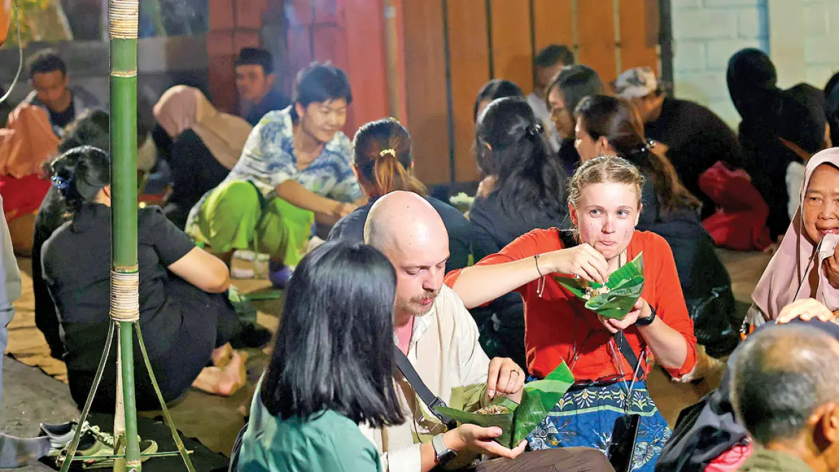 Sejumlah turis asing ikut menikmati nasi tumpeng di Desa Kemiren, Kecamatan Glagah pada Kamis malam (21/5). (Dini for Radar Banyuwangi)