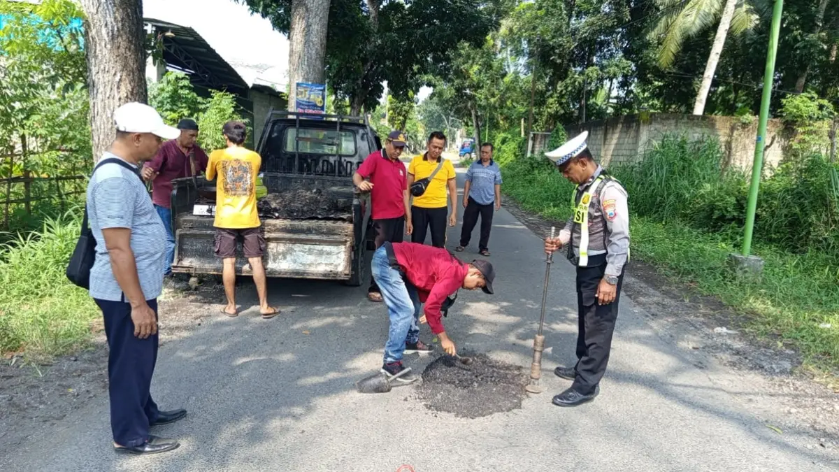 Anggota Polsek Kabat kerja bakti menambal jalan yang rusak di sebelah utara Jembatan Tambong, Kabat, Rabu (3/6). (Humas Polresta Banyuwangi)