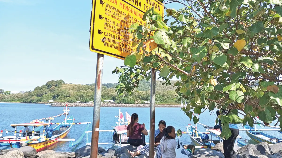 SIAP BERFUNGSI: Sejumlah warga menikmati suasana pesisir di bawah rambu peringatan kawasan rawan bencana di Pantai Grajagan pada Rabu (3/6). (Ismanto for Radar Banyuwangi)