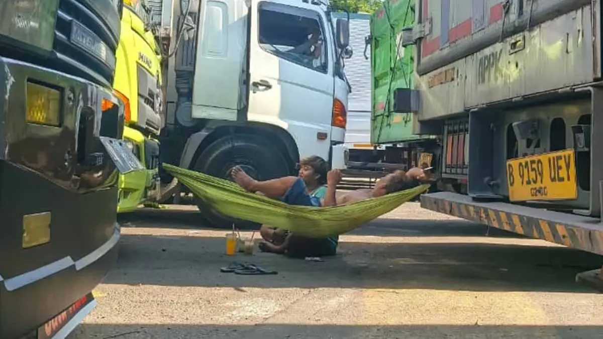 TUNGGU ANTREAN: Salah satu sopir truk logistik, Anton, bersantai di atas kain yang ia ikatkan di antara kedua sisi truk yang parkir di area Dermaga Bulusan, Sabtu (6/5). (Ksatria Raya/Radar Banyuwangi)