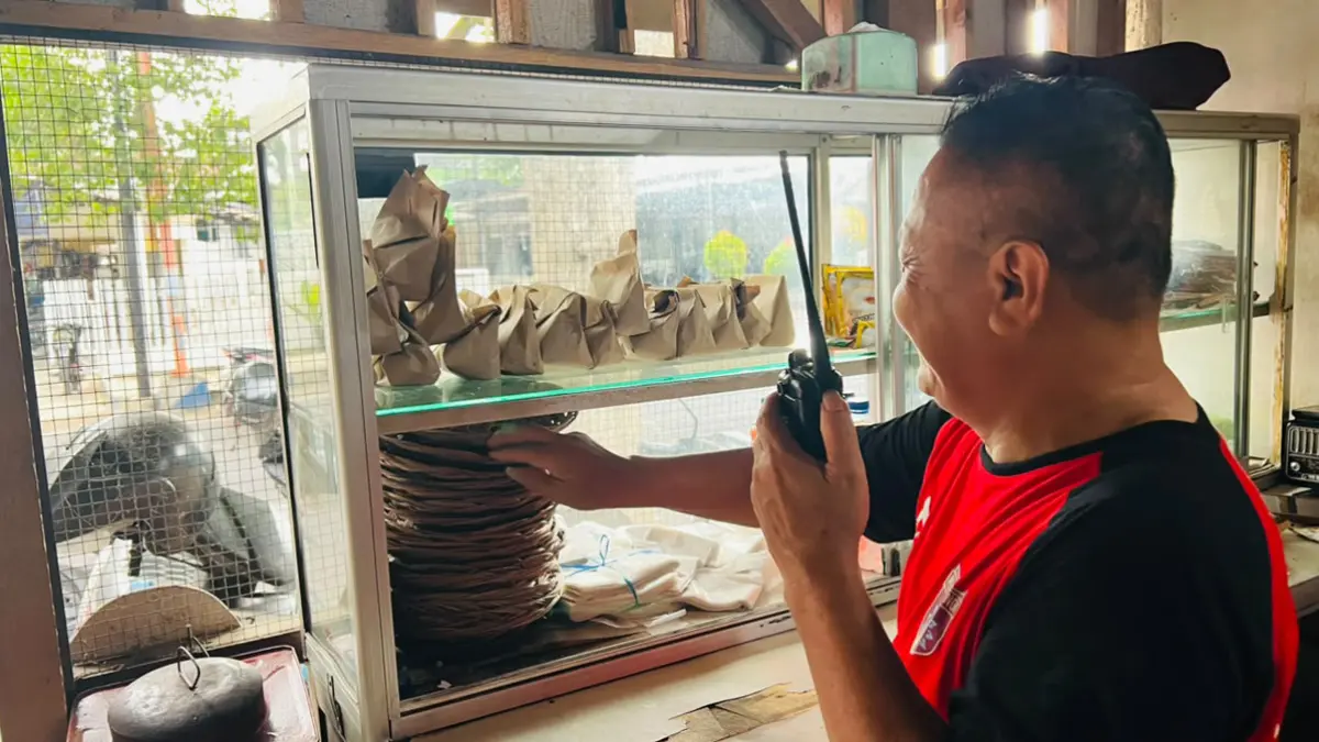 HEMAT WAKTU: Rojikin yang posisinya di warung berjarak 500 meter dari rumah, menghubungi istrinya lewat komunikasi walkie talkie agar disiapkan menu nasbung sesuai pesanan. (Bagus Rio/Radar Banyuwangi)