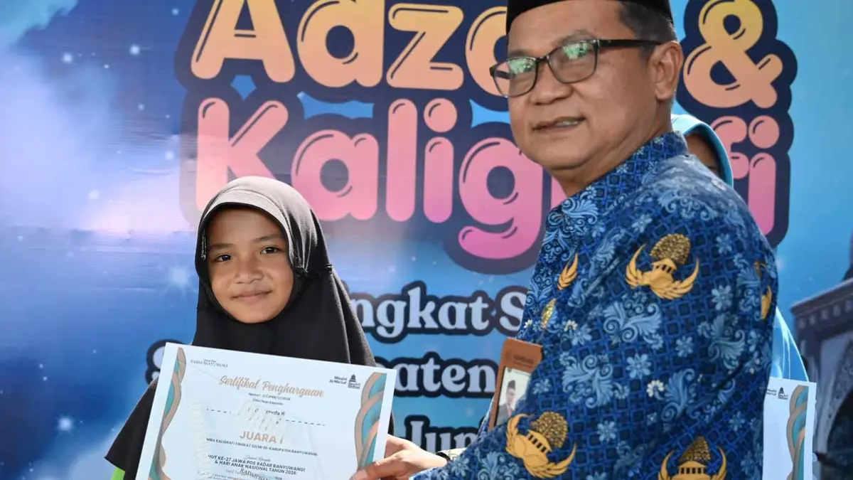 Kepala Kantor Kementerian Agama Banyuwangi Chaironi Hidayat meneyrahkan piala kepada juara 1 lomba kaligrafi Dzakia Arsyifa R dari MI Darul Ulum Muncar. (Ramada Kusuma/Radar Banyuwangi)