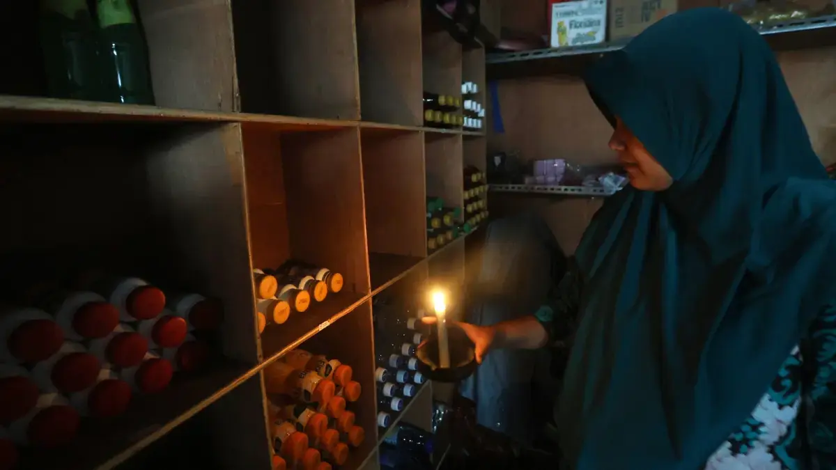 TIGA JAM PEMADAMAN: Zunaida, pemilik toko kelontong di Jalan Ikan Piranha, Kecamatan Blimbing menyalakan lilin untuk membantu penerangan, kemarin siang (19/6). (Darmono/Radar Malang)