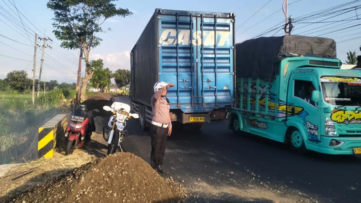 Anggota Satlantas Polresta Banyuwangi mengatur arus lalin di jalan raya Desa Bengkak, Wongsorejo saat berlangsung perbaikan jalan, Sabtu (11/7). (Marwanto for Radar Banyuwangi)