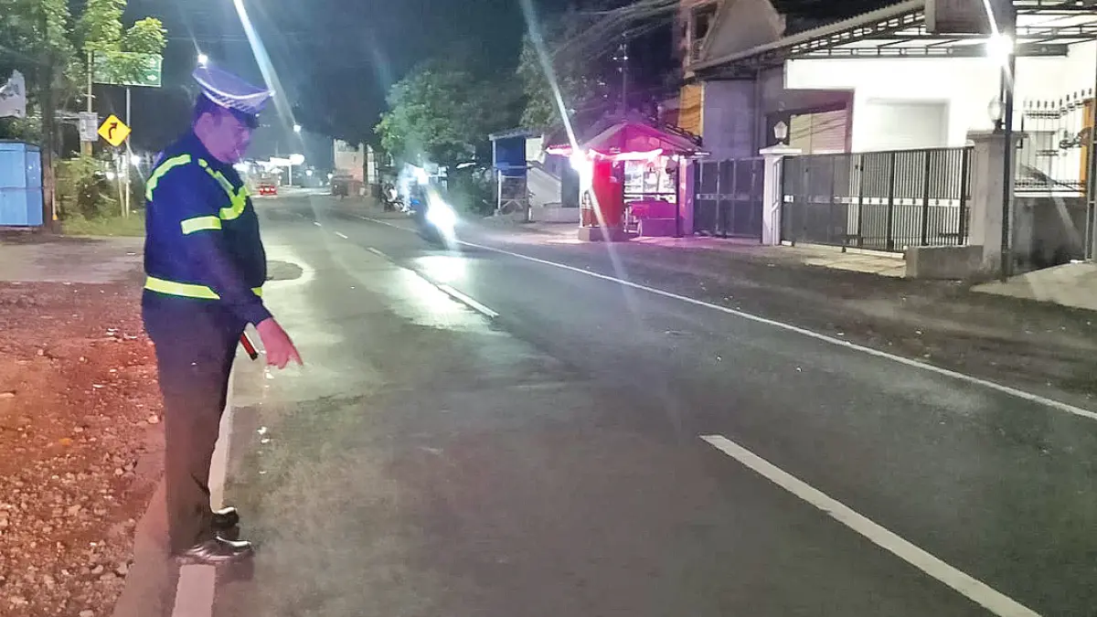 Anggota Polsek Genteng menunjukkan lokasi kecelakaan yang melibatkan pengendara sepeda motor dan pejalan kaki di Jalan Raya Hasanudin, Kecamatan Genteng, Minggu malam (12/7). (Dedy for Radar Banyuwangi)