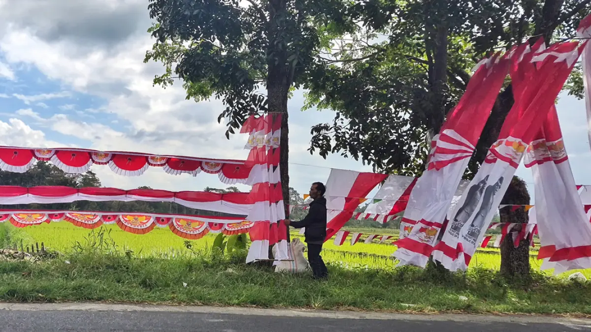 Adib Sofyan, 47, asal Kabupaten Bandung, Jawa Barat, menata bendera dagangannya di tepi jalan Dusun Maron, Desa Gentengkulon, Kecamatan Genteng, Rabu (22/7). (Salis Ali/Radar Banyuwangi)