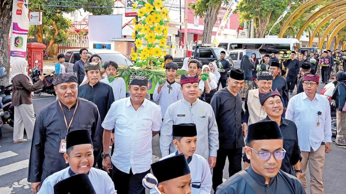 Plt Kepala Dispendik Alfian (kiri, pakai udeng) mengikuti arak-arakan ancak dan jodang telur hias pada rangkaian Festival Padang Ulanan Kecamatan Banyuwangi di kawasan Taman Blambangan, Jumat (24/7). (Ramada Kusuma/Radar Banyuwangi)