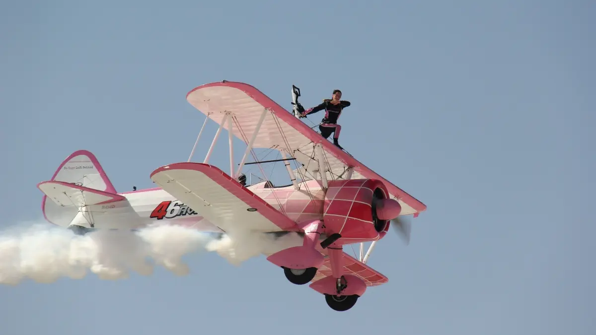 Penampil wing walking berdiri di atas sayap pesawat biplan saat melakukan atraksi udara. Aksi ekstrem ini mengandalkan keberanian, ketangkasan, dan prosedur keselamatan ketat. (Pexels/bora kocak)