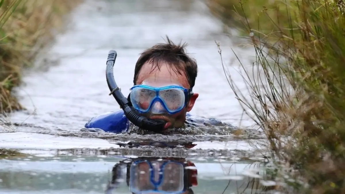 Peserta Bog Snorkelling berjuang melintasi parit gambut dalam perlombaan unik di Llanwrtyd Wells, Wales. Olahraga ini mengandalkan snorkel dan kaki katak tanpa diperbolehkan menggunakan gaya renang konvensional. (Visit Wales)