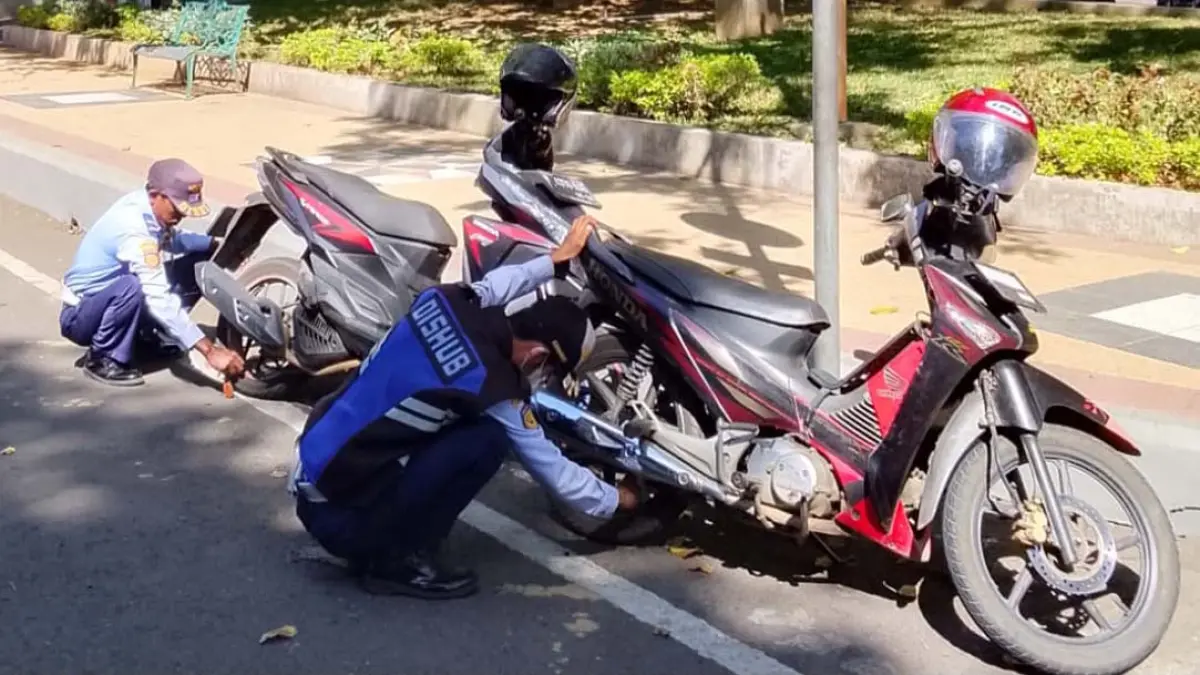 Anggota Dishub Banyuwangi menggembosi sepeda motor yang parkir sembarangan di Taman Sritanjung, Sabtu (15/8). (Bagus Rio/Radar Banyuwangi)