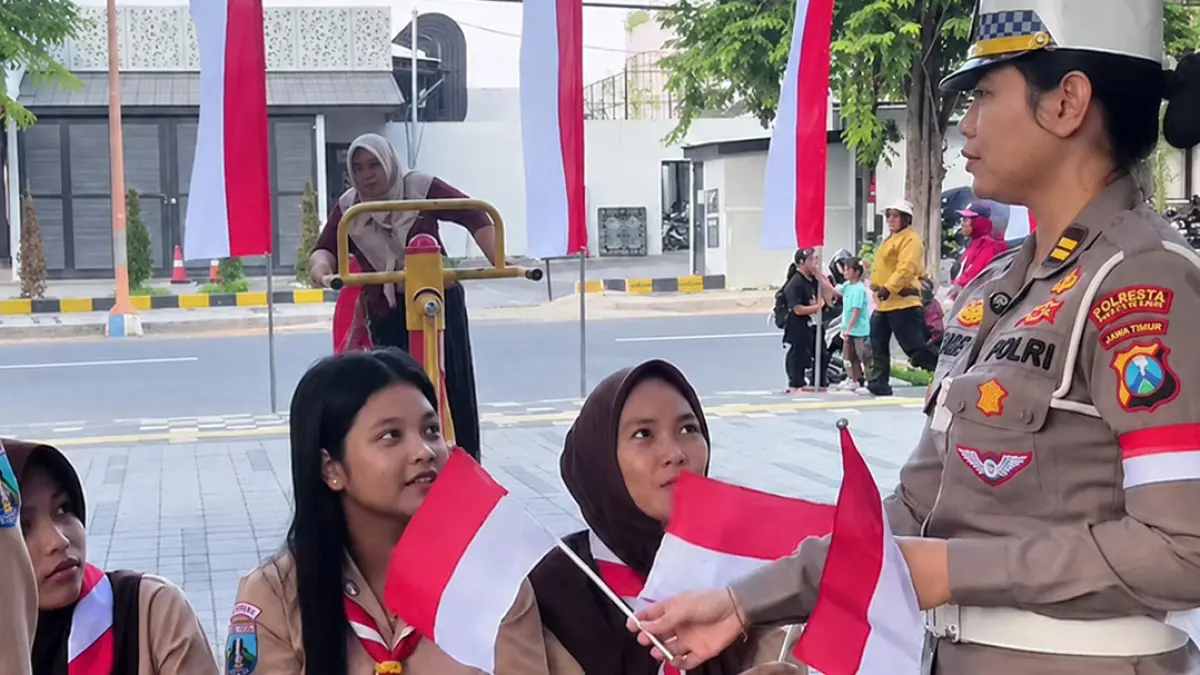 Plt Kasi Humas Polresta Banyuwangi Iptu I Made Chandra membagikan bendera Merah Putih kepada pelajar berseragam Pramuka di sekitar Taman Blambangan, Senin (18/8). (Humas Polresta Banyuwangi)