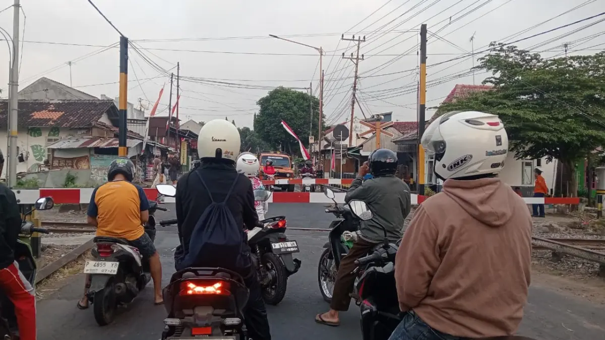 Pengendara sepeda motor berhenti di belakang palang pintu saat kereta api melintas. Disiplin menunggu hingga palang terbuka menjadi bagian penting dari keselamatan di perlintasan sebidang. (Balquisse untuk Radar Banyuwangi)