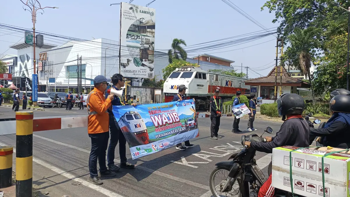 Kereta api melintas di perlintasan sebidang saat palang pintu tertutup. KAI Daop 8 Surabaya memperkuat pengamanan dan mengimbau pengguna jalan tidak menerobos perlintasan demi mencegah kecelakaan. (KAI)