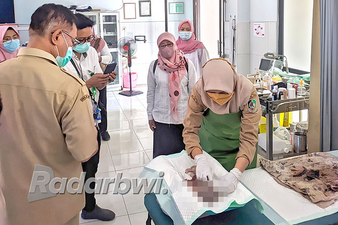 TEGA: Petugas medis dari Puskesmas Kedungrejo membersihkan mayat bayi laki-laki yang baru ditemukan di di jembatan Dusun Krajan, Desa Kedungrejo, Kecamatan Muncar, Selasa (7/6). (Salis Ali/Radar Genteng)