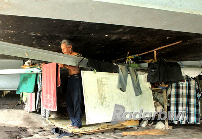 RUMAH: Agus Santoso di tempat tinggalnya, di kolong Jembatan Setail, Desa Genteng Kulon, Kecamatan Genteng, Minggu (3/7). (Salis Ali/Radar Genteng)