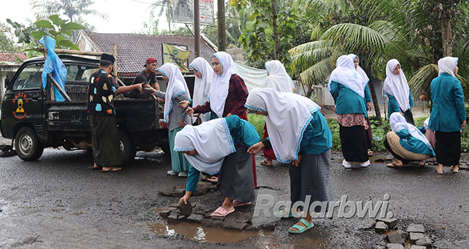 TUTUP PAVING: Para santri Pondok Pesantren Darussalam Blokagung menambal jalan raya di Desa Karangdoro dan Karangmulyo, Kecamatan Tegalsari yang rusak dengan paving, Selasa (12/7) lalu. (Irham Muzaki/Radar Genteng)