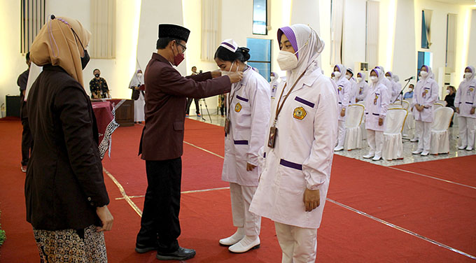 SIMBOLIS : Ketua Stikes Banyuwangi Dr H Soekardjo didampingi Ketua Prodi Sarjana Kebidanan Desi Trianita SST M.Kes mengalungkan tanda pengenal kepada perwakilan mahasiswa kebidanan sebagai simbol penyematan tanda praktik lahan kebidanan, Senin (25/7).