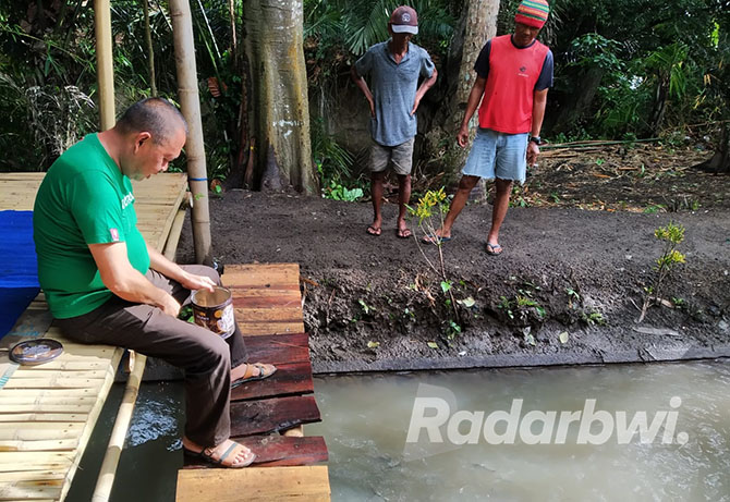 MENEBAR: Wawan ditemani sejumlah warga memberikan makan ikan patin di Desa Bomo, Kecamatan Blimbingsari, Minggu (9/10). (Gareta Wardani/Radar Banyuwangi)