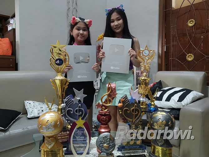 PRESTASI GEMILANG: Cherie (kanan) dan Vivi menunjukkan silver play button dan beberapa piala dari kejuaraan lomba olah vokal. (Gareta Wardani/Radar Banyuwangi)