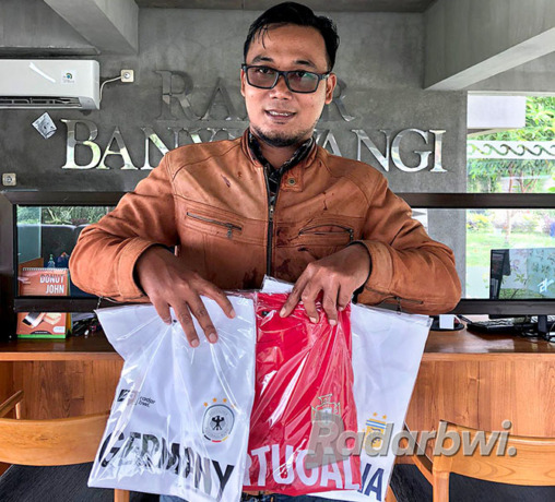 MURAH BANGET: Erlang Wisnu Adi memborong tiga kaus timnas Piala Dunia di kantor Jawa Pos Radar Banyuwangi, Jumat (18/11). (AULINA TIASIH/RaBa)