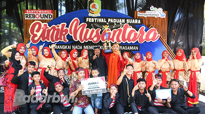 PRESTISIUS: Kepala SMPN 1 Glenmore Ahmad Hasan (tengah)  bersama grup paduan suara SMPN 1 Glenmore mengangkat trophy usai dinobatkan juara terbaik satu dalam Festival Paduan Suara Etnik Nusantara, Kamis (8/12). (Ramada Kusuma/Radar Banyuwangi)