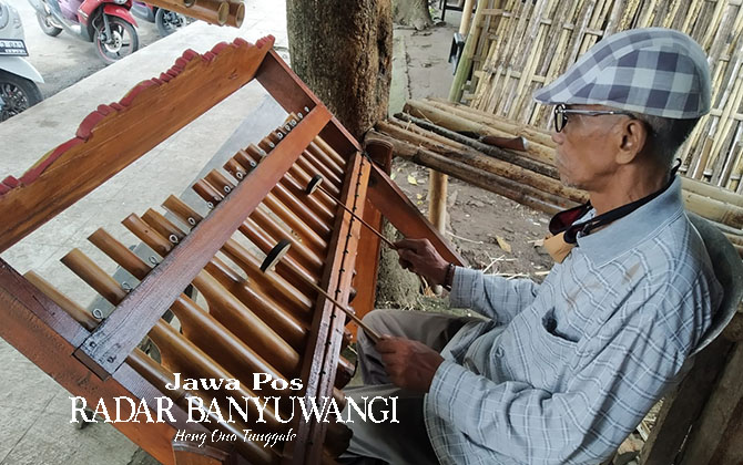 BERHARAP ADA PENERUSNYA: Sutoyo memainkan angklung hasil karya sendiri di kios alat musik tradisional yang terletak di Jalan Letkol Istiqlah, Banyuwangi, Kamis (2/2). (Gareta Wardani/Radar Banyuwangi)