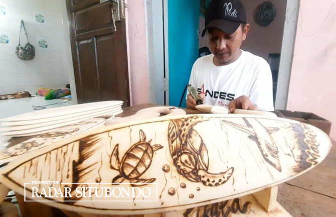 KREATIF: Fatwa Dewantoro menunjukkan hasil produksi Pirografi yang dibuat pada papan kayu dengan menggunakan solder, di Desa Kilensari, Kecamatan Panarukan, Minggu (12/3). (Iwan Feriyanto/Radar Situbondo)