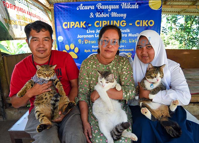 PENUHI NAZAR: Pasutri Bokiyanto dan Indrawati bersama anak semata wayangnya, Kharisma, menggendong Cipak, Cipung, dan Ciko dalam pesta khitan kucing di Desa Kluncing, Senin (29/5). (Ramada Kusuma/RadarBanyuwangi.id)